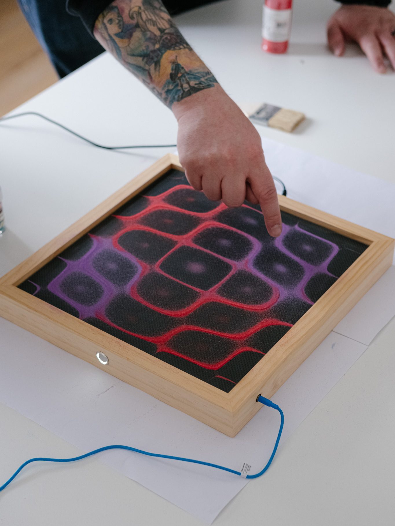 Sam Thomas pointing to a colourful pattern generated on a Chaladni Plate